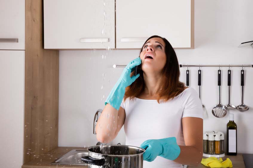 Shocked Woman Calling Plumber While Collecting Water Leaking From Ceiling Using Utensil