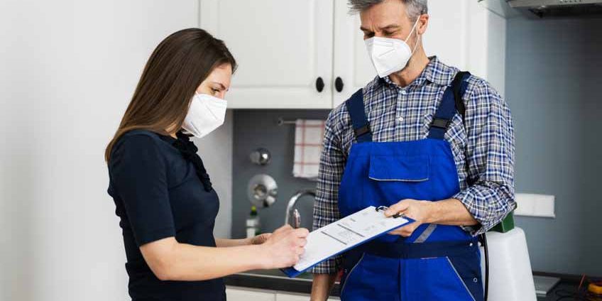 Handyman Plumber And Customer With Service Contract Handyman Plumber And Customer With Service Contract On Clipboard In Face Mask