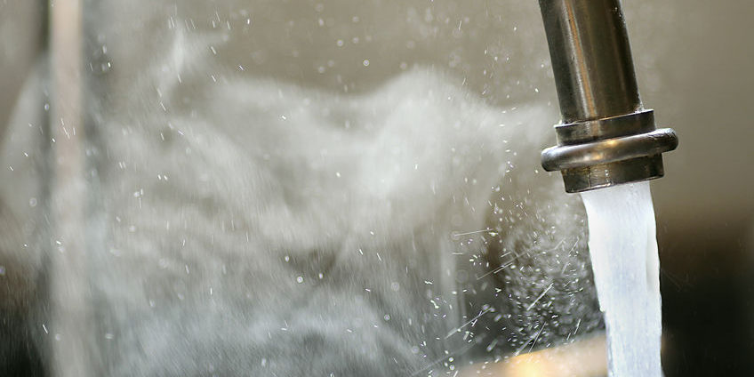 Hot Steaming Water Running from Kitchen Faucet Hot steaming running tap water is pouring out of a stainless steel kitchen faucet.